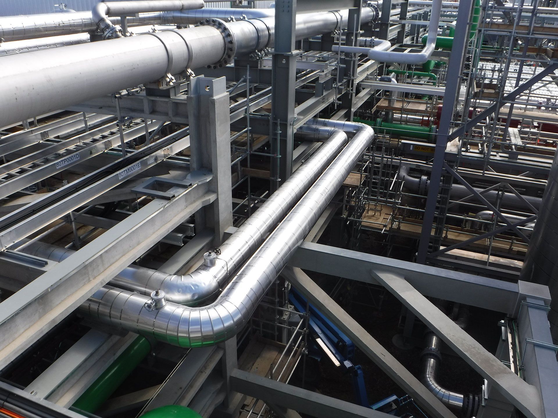Industrial pipes and metal catwalks in a crowded plant, with shiny silver tubing and steel supports.