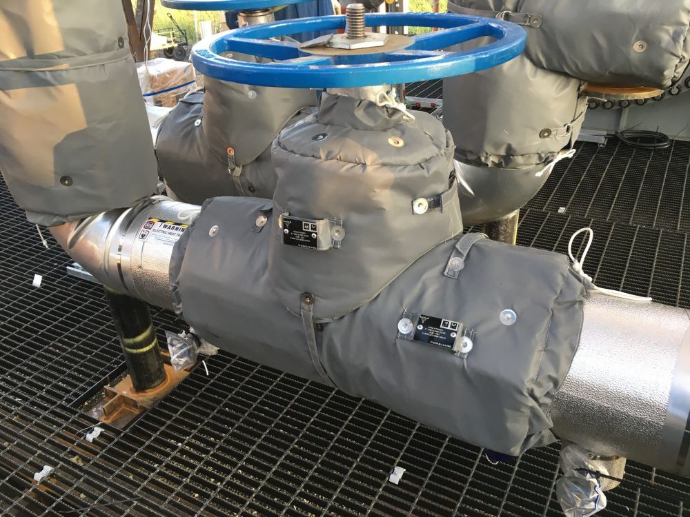 Insulated industrial pipes and valves with gray covers and a blue handwheel in a mechanical room