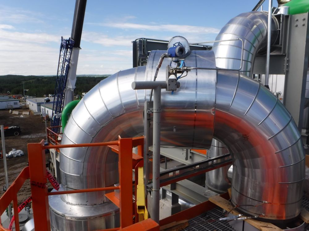Large silver industrial pipes with orange supports at a construction site under a blue sky