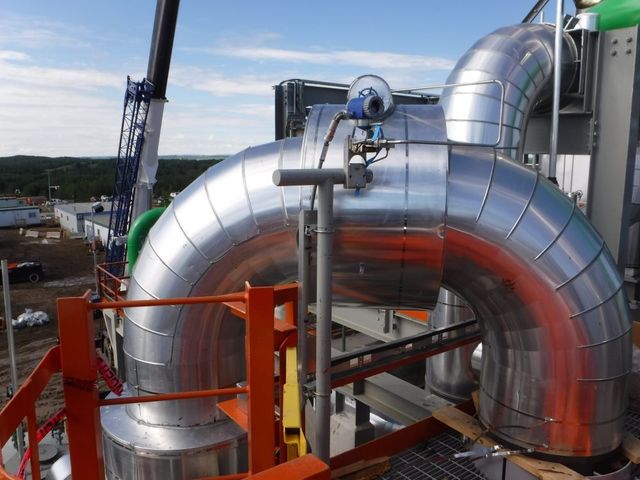Large silver industrial pipes and ducts at a construction site under a blue sky