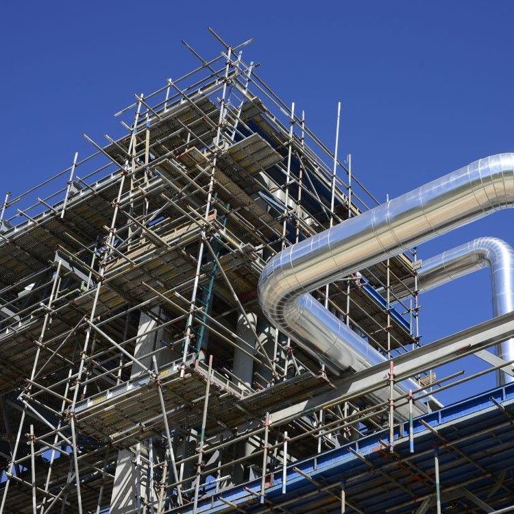 Industrial scaffolding beside large silver pipes under a clear blue sky