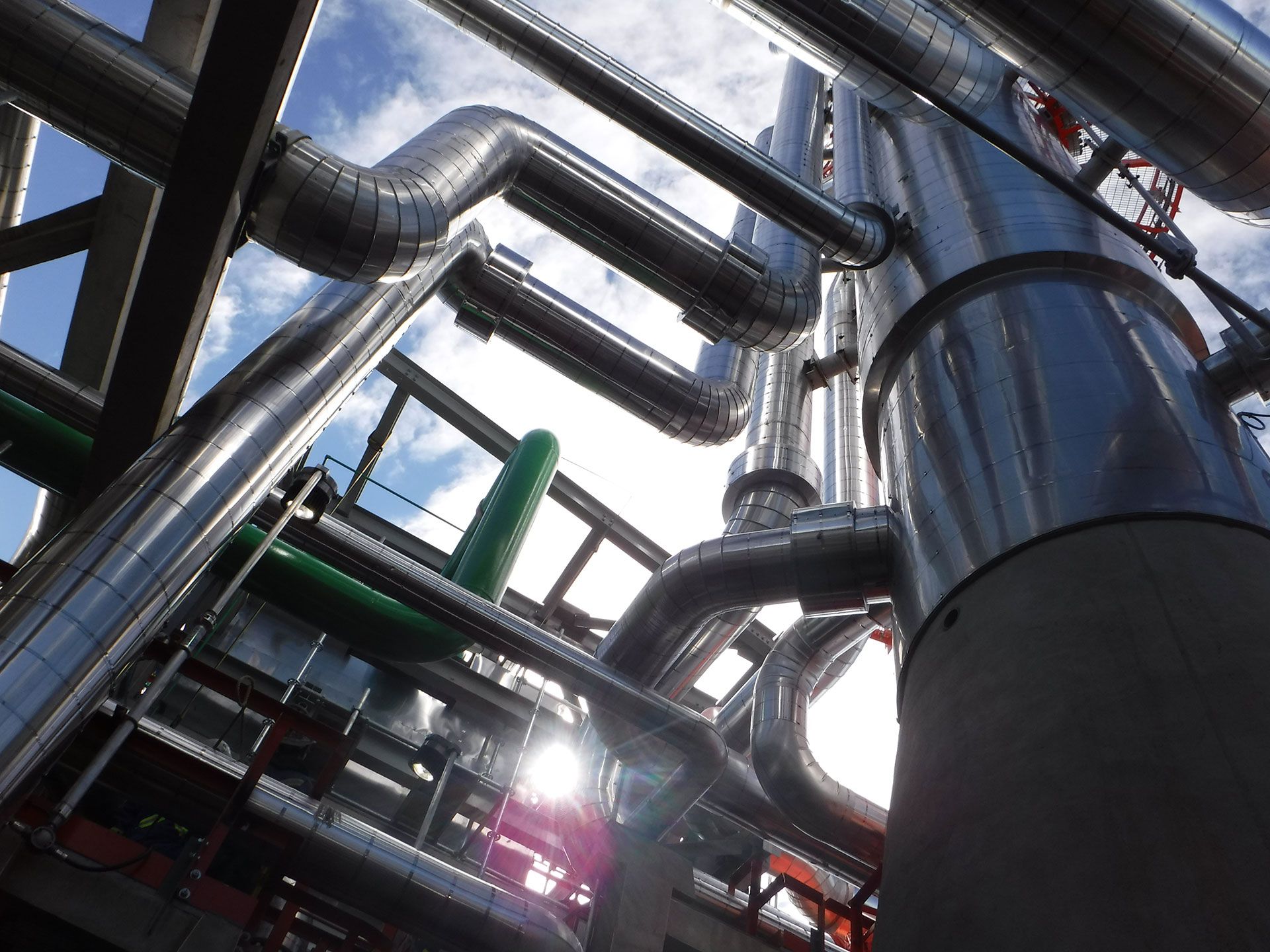 Industrial pipes and metal tanks in a factory, shot from a low angle with sunlight reflecting off steel surfaces