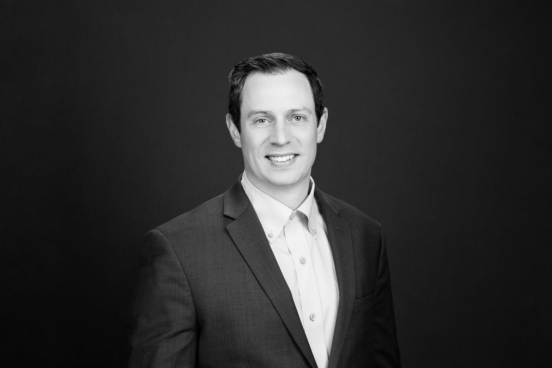 Studio portrait of a smiling man in a dark suit against a black background