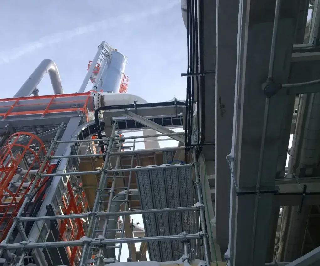 Industrial steel structure with red and gray scaffolding beside a tall platform under a cloudy sky
