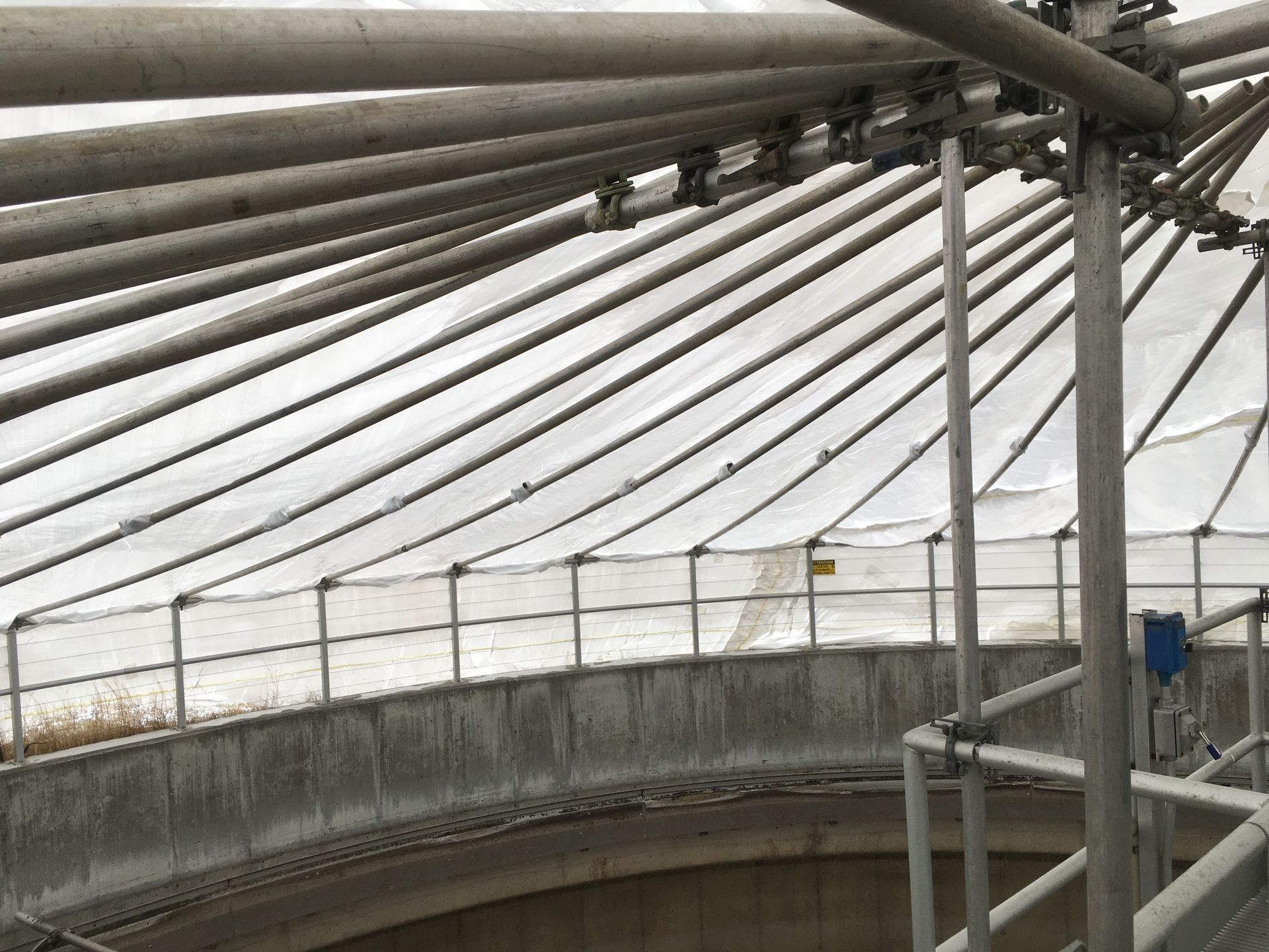 Curved metal pipes and beams inside a covered industrial structure with a gray translucent roof