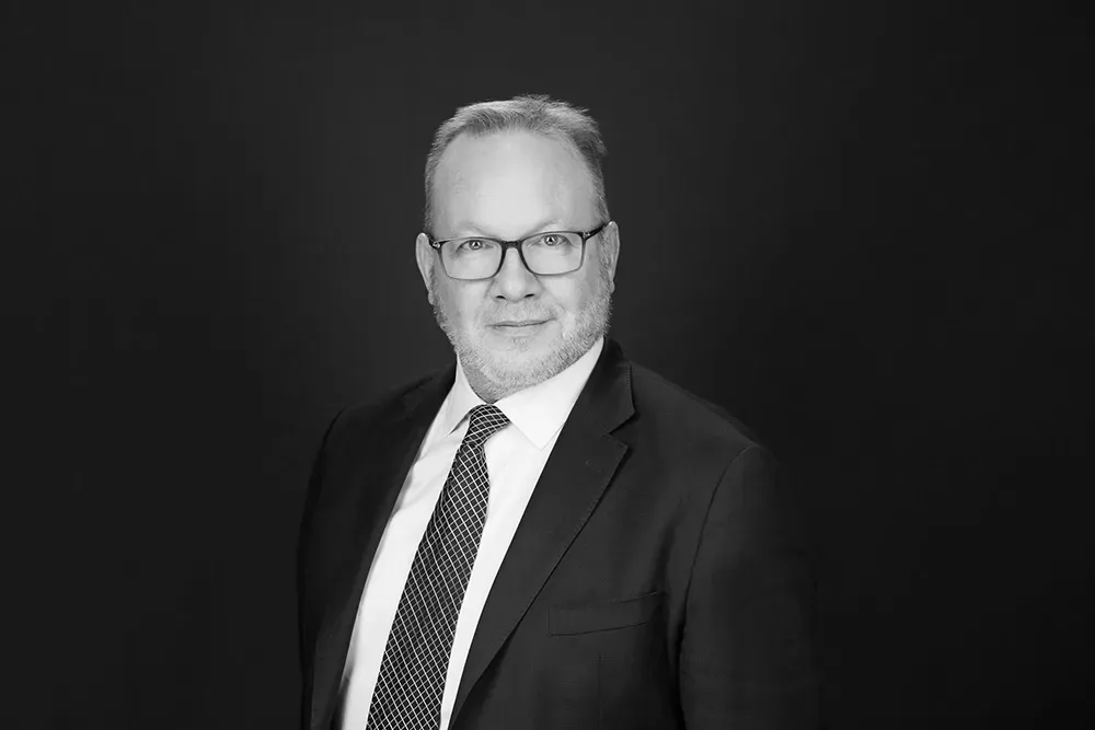 Studio portrait of a man in a dark suit and tie against a black background.