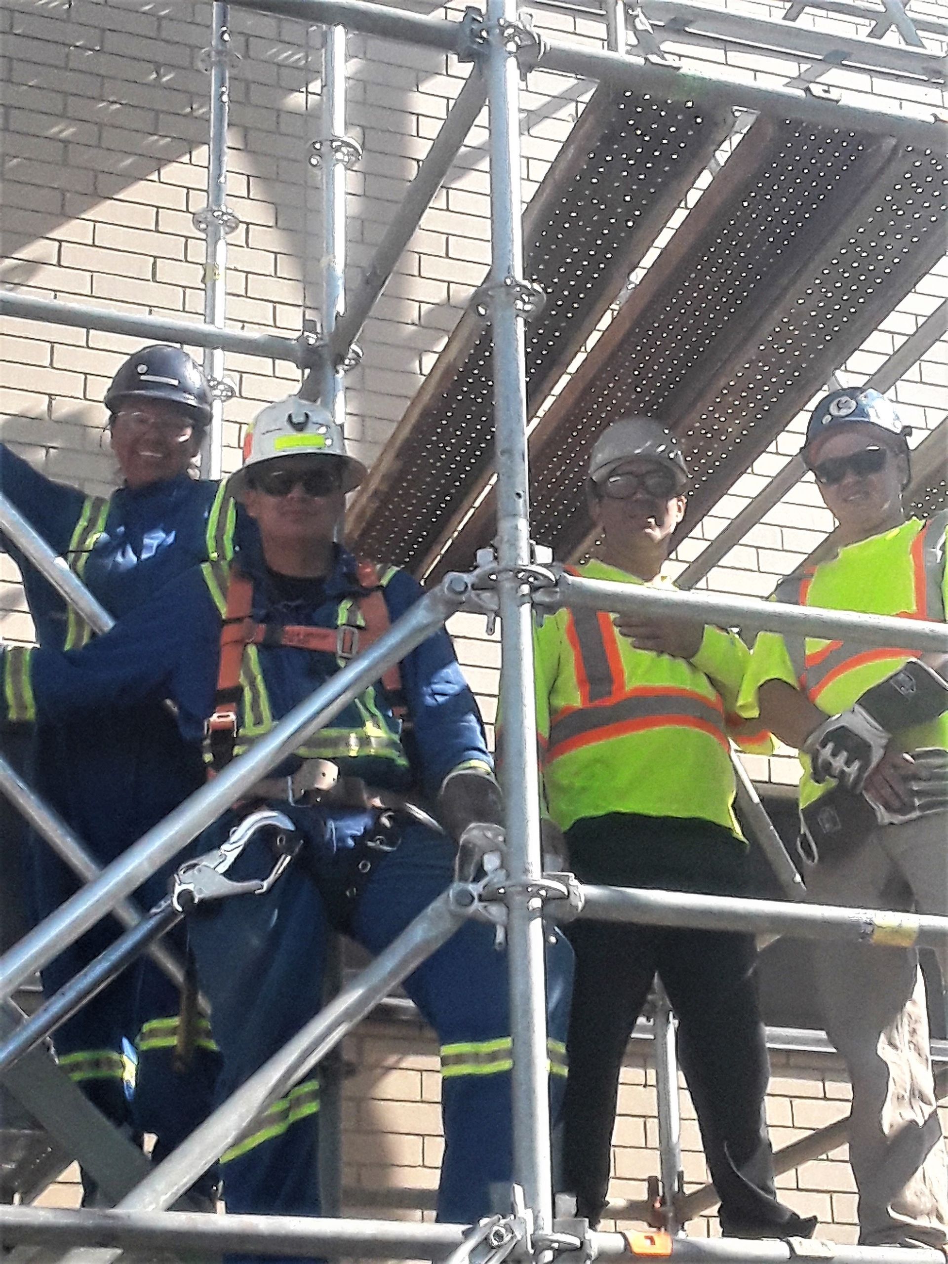 Workers in safety vests and helmets standing on scaffolding beside a metal structure