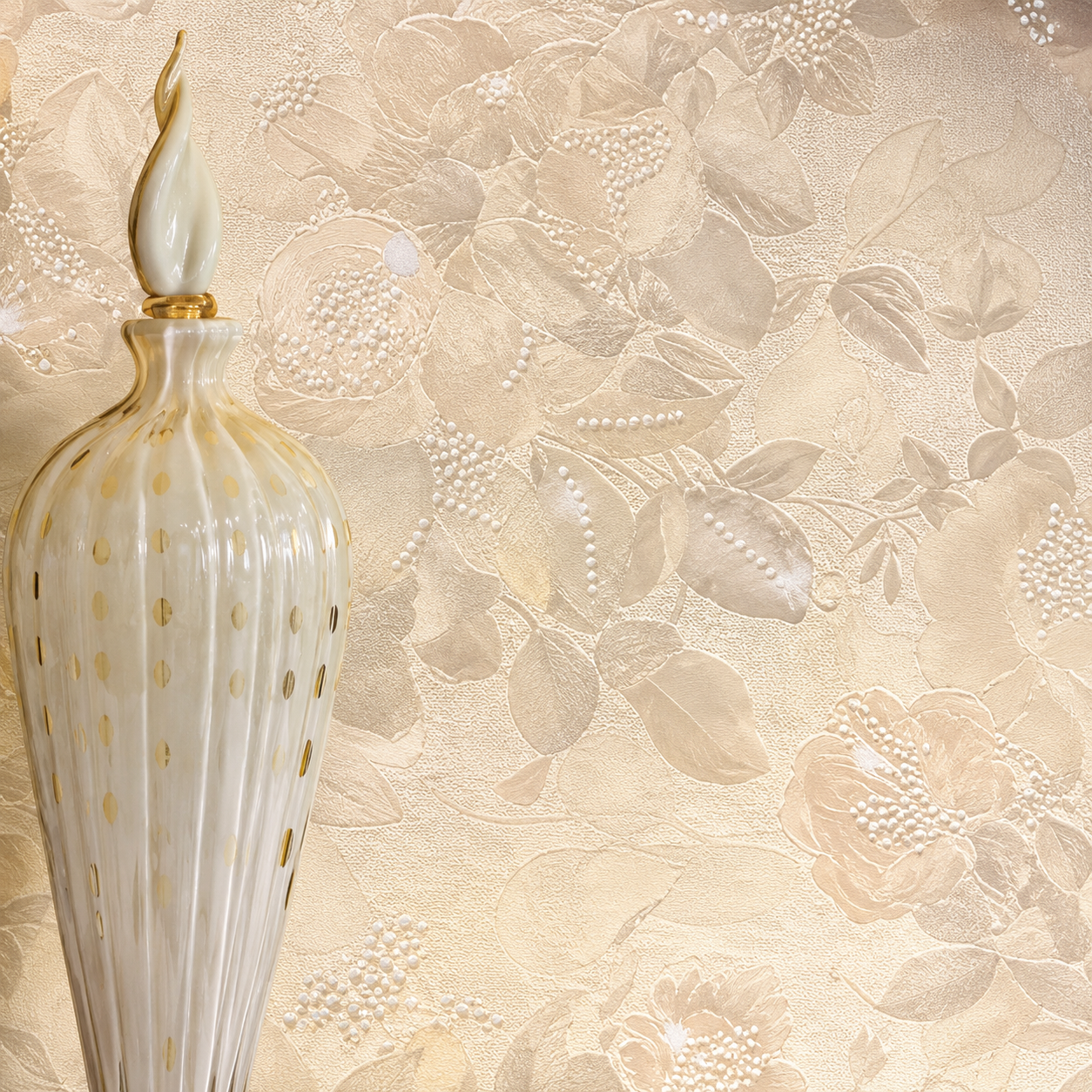 Vaso decorativo bianco con dettagli dorati su uno sfondo murale color crema con texture floreale.