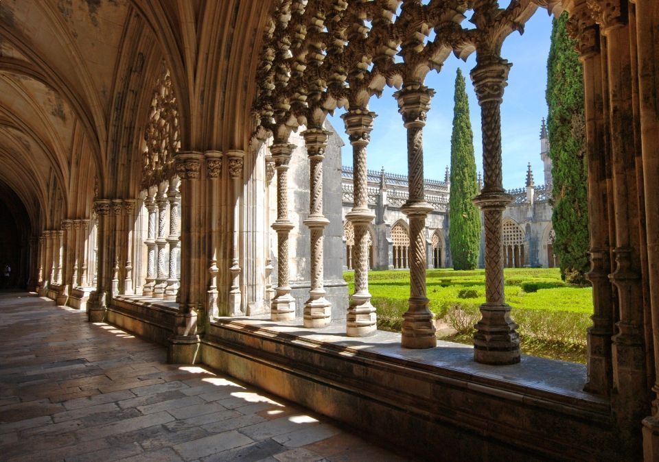 Chiostro soleggiato con archi e colonne in pietra affacciato su un cortile verde.