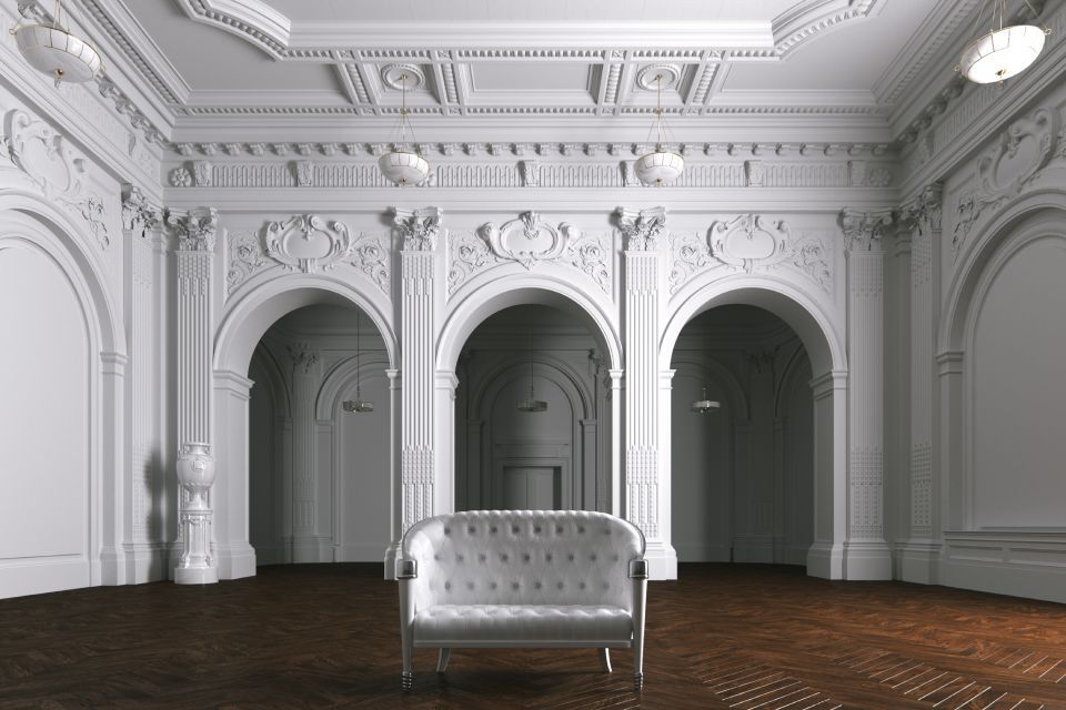 Elegante interno bianco con archi decorati, lampadario e divano capitonné su un pavimento in legno scuro.