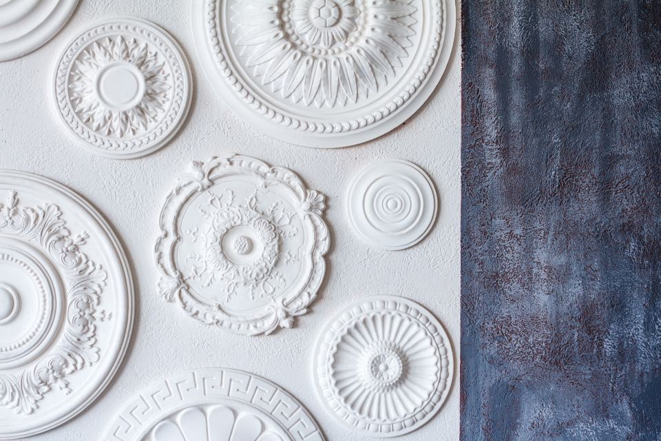 Rosoni decorativi bianchi sul soffitto, su una parete accanto a un pannello blu scuro con superficie ruvida.