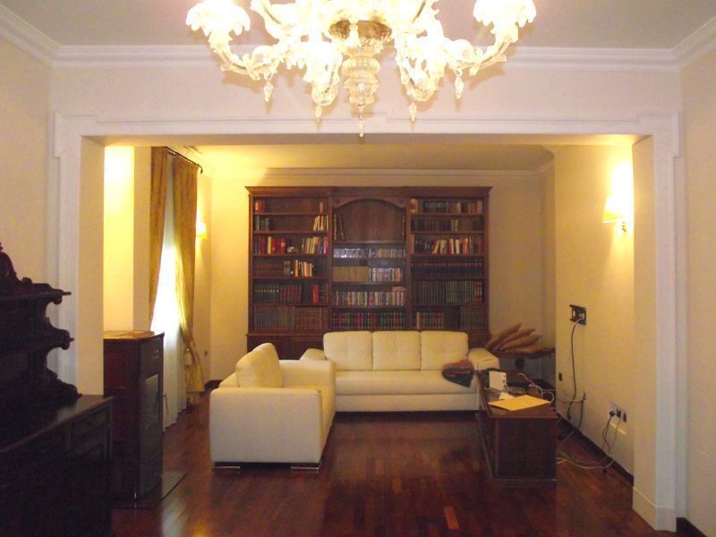 Elegante soggiorno con divani bianchi, libreria e lampadario, visibile attraverso un ampio arco.