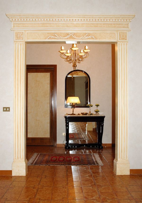 Elegante corridoio con finiture color crema, lampadario, specchio, consolle e pavimento in legno.