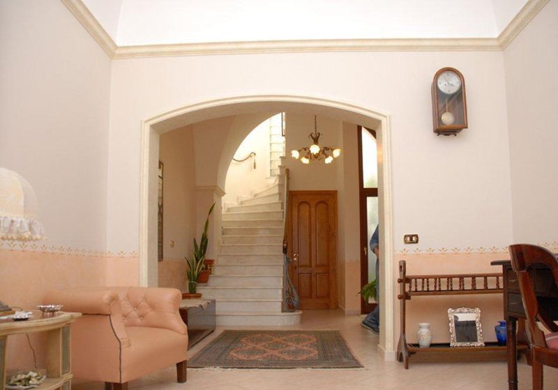 Luminoso atrio con porta ad arco, scala, orologio a muro e poltrone color pesca in un ambiente interno beige.