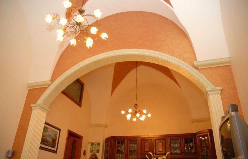 Stanza dai toni caldi con un'ampia porta ad arco, lampade a sospensione, quadri incorniciati alle pareti e armadi in legno.