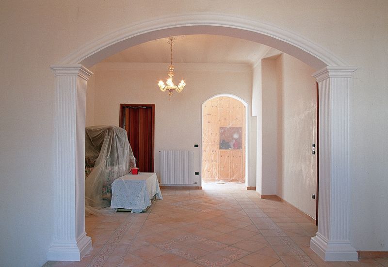 Stanza vuota con porta ad arco, lampadario e mobili rivestiti in un interno piastrellato.