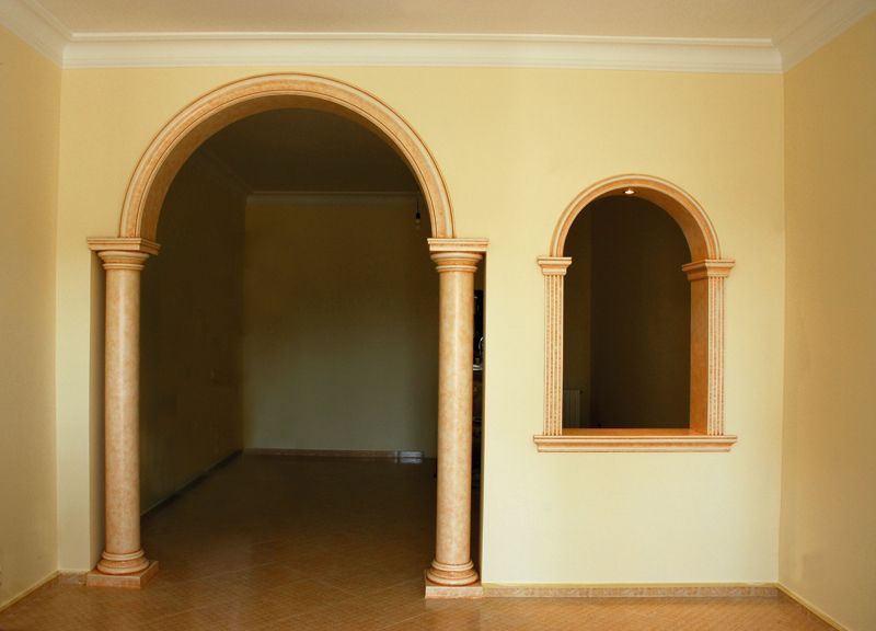 Stanza vuota con pareti beige, pavimento in legno e due porte ad arco, una grande e una piccola.