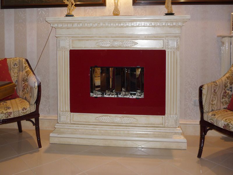 Camino decorativo bianco con inserto rosso in un salotto formale, fiancheggiato da poltrone decorate.