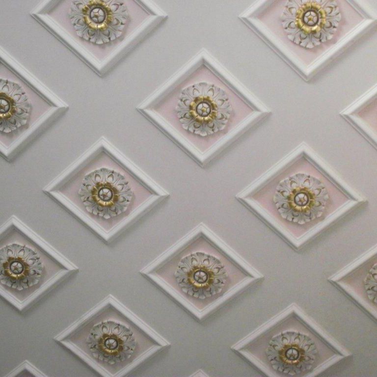 Parete grigia con pannelli decorativi a forma di diamante ornati da medaglioni floreali dorati.