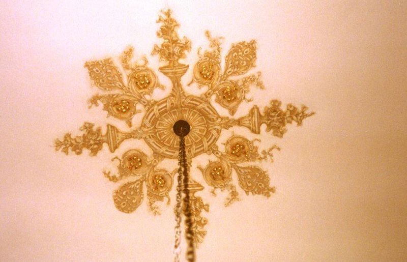 Decorazione murale ornamentale dorata a forma di fiocco di neve con asta centrale su una parete chiara