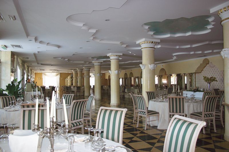 Elegante sala da pranzo con sedie a righe, colonne bianche e tavoli apparecchiati in un luminoso ingresso.