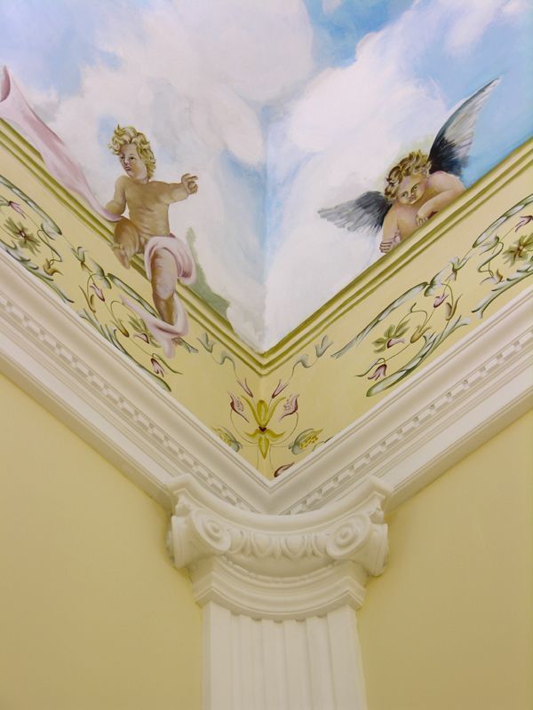 Angolo del soffitto dipinto con putti e decorazioni floreali sopra una colonna decorativa bianca
