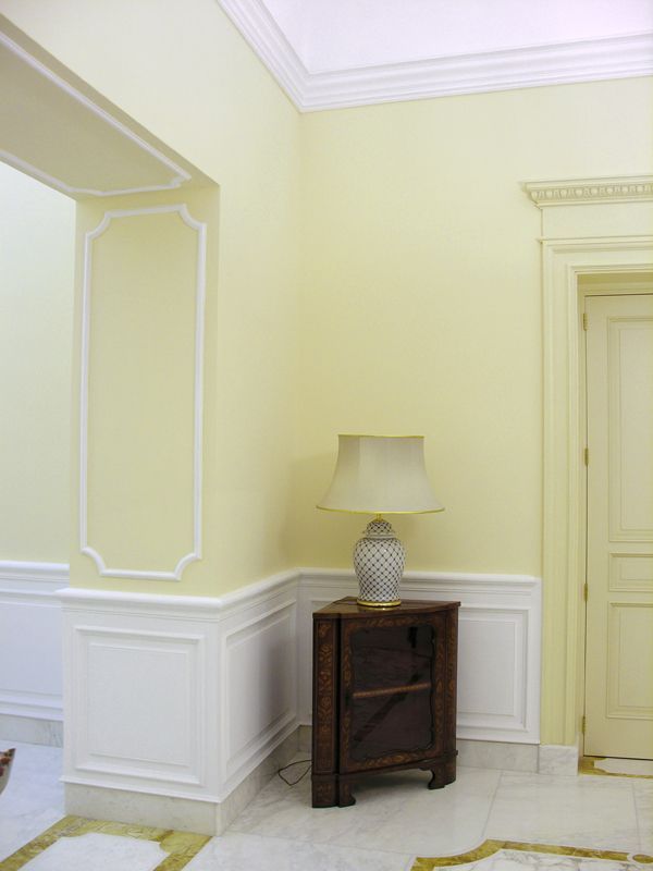 Elegante angolo corridoio beige con finiture bianche, tavolino scuro e lampada accanto a una porta chiusa.