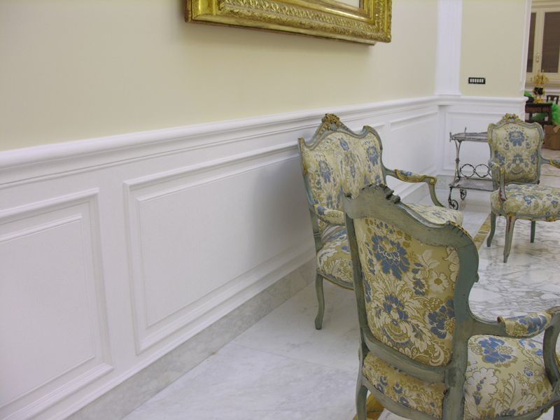 Eleganti sedie rivestite con motivi floreali in una stanza luminosa con boiserie bianca e tappeto decorato.