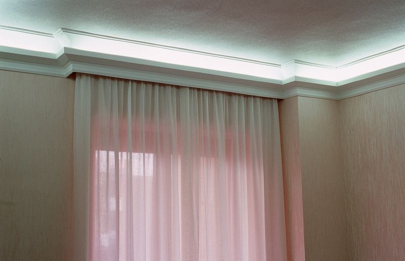 Finestra con tende trasparenti rosa tenue e illuminazione a incasso sul soffitto in una stanza dai toni neutri.