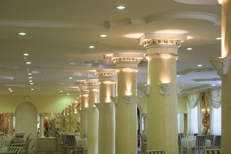 Elegante sala per banchetti con colonne color crema, luci calde e decorazioni ad arco.