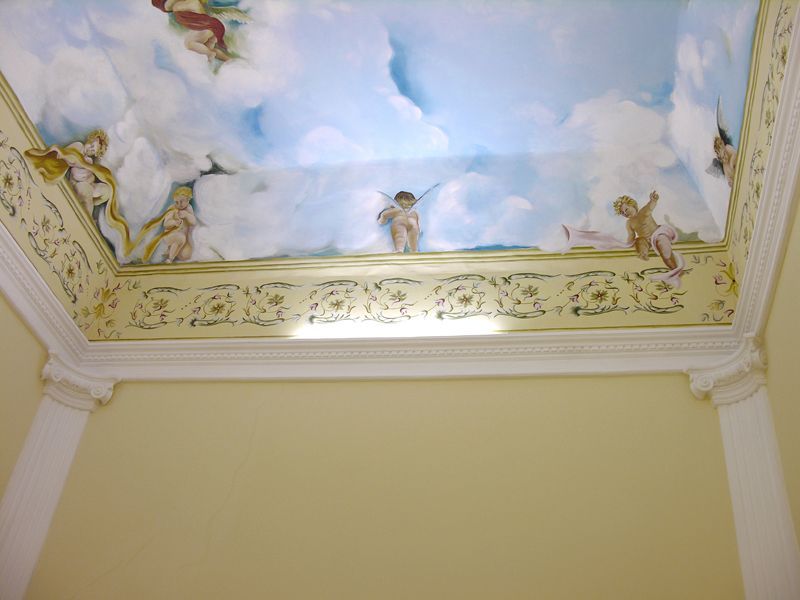 Affresco decorativo sul soffitto con nuvole, angeli e ornate decorazioni dorate sopra una parete chiara