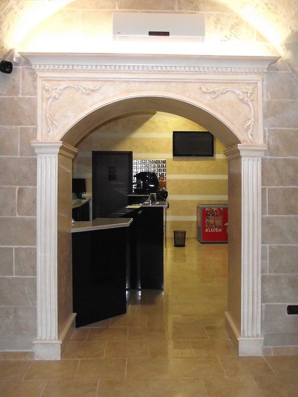 Un elaborato arco in pietra incornicia l'ingresso della hall dell'hotel, con pavimenti in pietra color beige lucido e un bancone della reception nero all'interno.