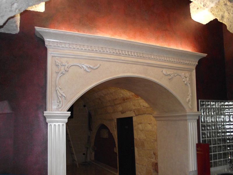 Camino ad arco bianco decorato con colonne in una stanza poco illuminata