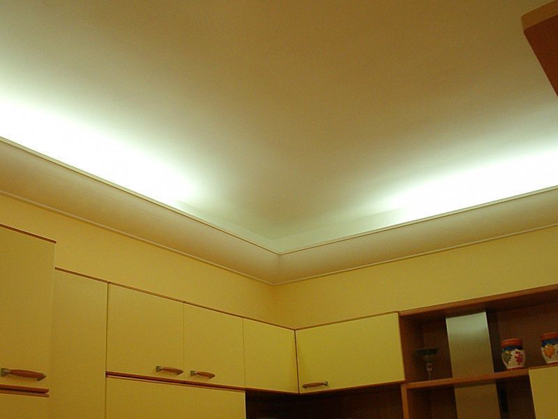 Cucina con soffitto e pensili illuminati da una luce calda, con una mensola sulla destra.