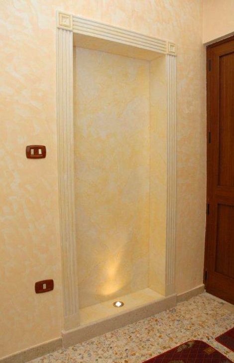 Nicchia a muro con illuminazione a incasso in una stanza beige, accanto a una porta di legno.