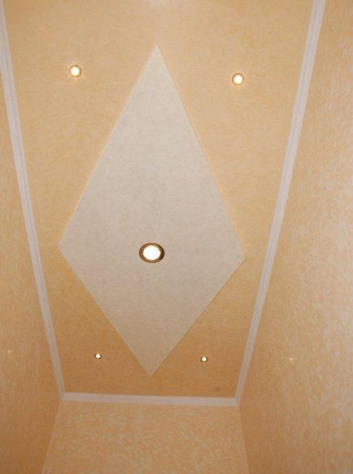 Soffitto con un grande disegno bianco a forma di diamante e faretti a incasso su sfondo beige.