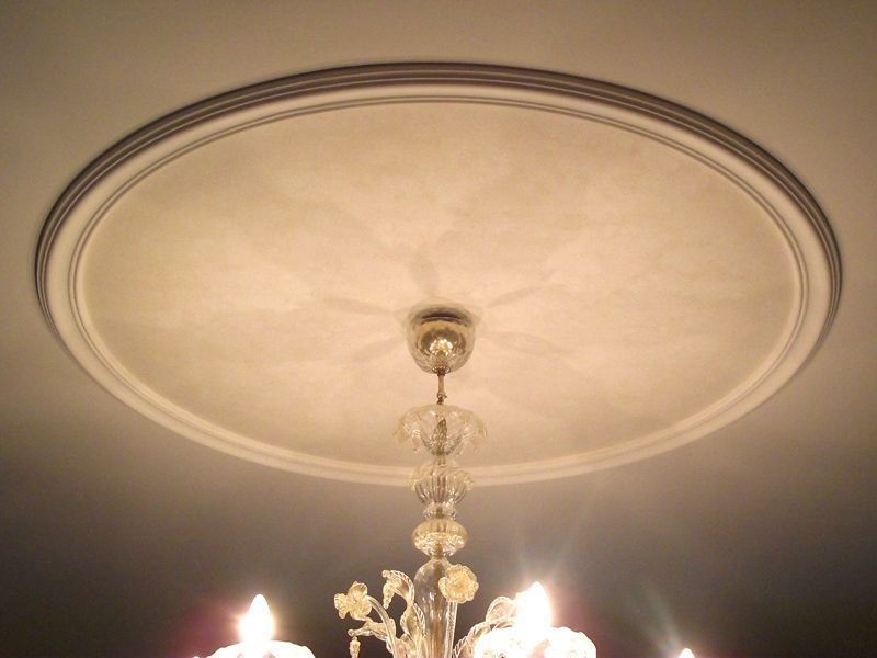 Lampadario sospeso a un elaborato rosone sul soffitto, con candele accese al di sotto.