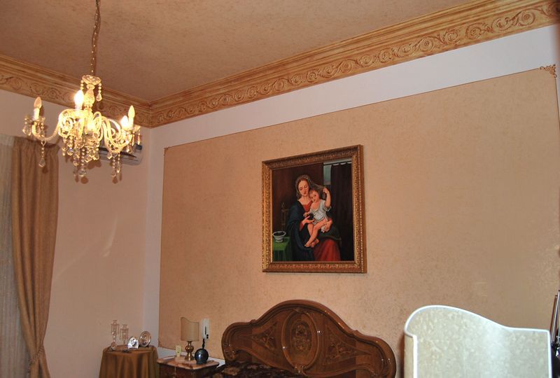 Camera da letto con lampadario, testiera intagliata e ritratto incorniciato su una parete beige.