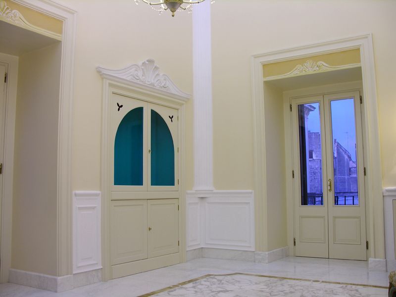 Elegante stanza vuota con pareti color crema, finiture bianche e due alte porte ad arco con vetri leggermente azzurri.