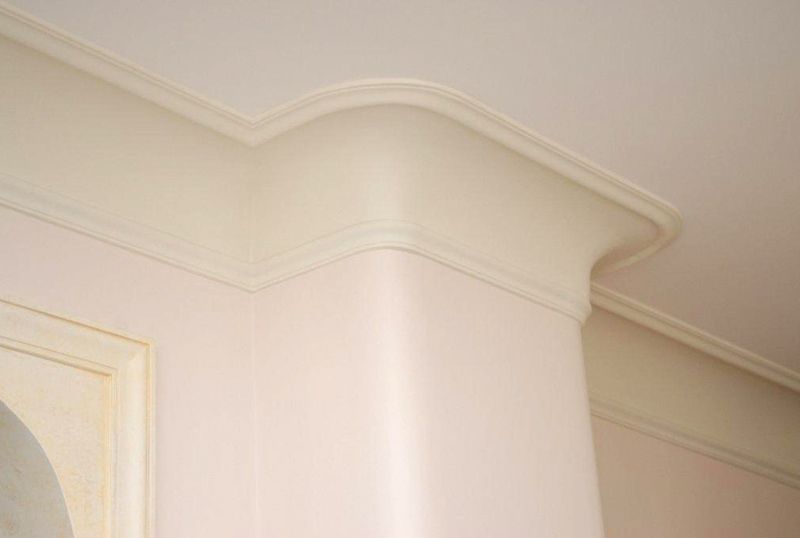 Cornice decorativa bianca per il soffitto e modanatura angolare curva in una stanza illuminata da una luce soffusa.