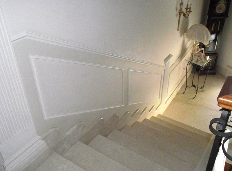 Scala con pareti e ringhiera bianche che scende verso un pianerottolo, illuminata da una morbida luce interna.