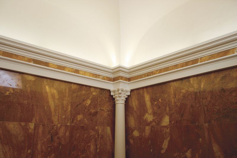 Angolo in marmo con elaborate decorazioni dorate e colonna bianca sotto un soffitto a volta.