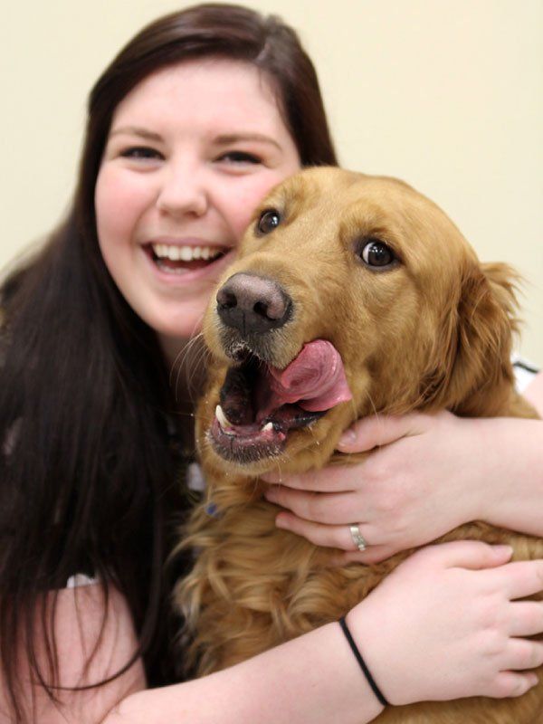 Woman hugging a golden retriever, both smiling, dog licking its nose.