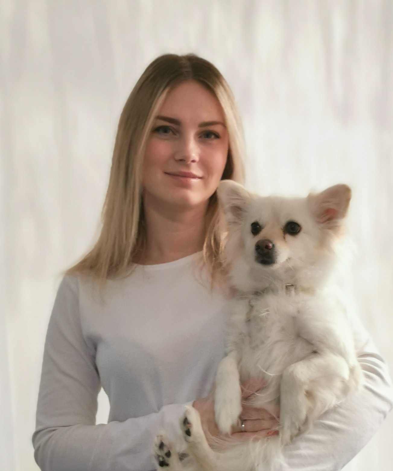 Woman with long blonde hair holding a small white dog; both looking at the camera.