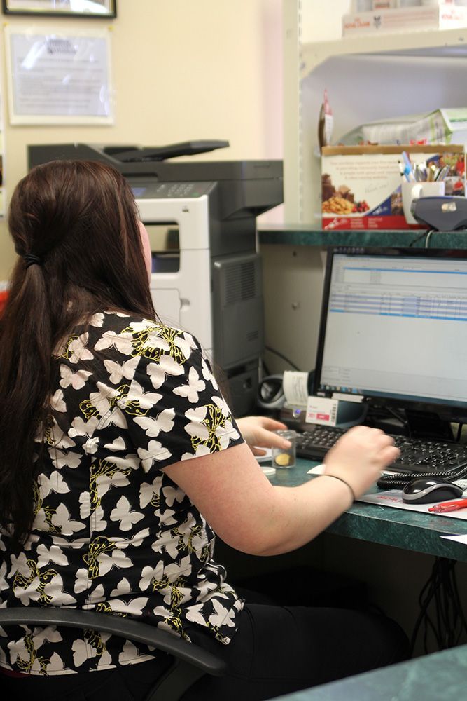 Person at a desk, typing on a computer. She wears a butterfly print shirt and sits in front of a printer.