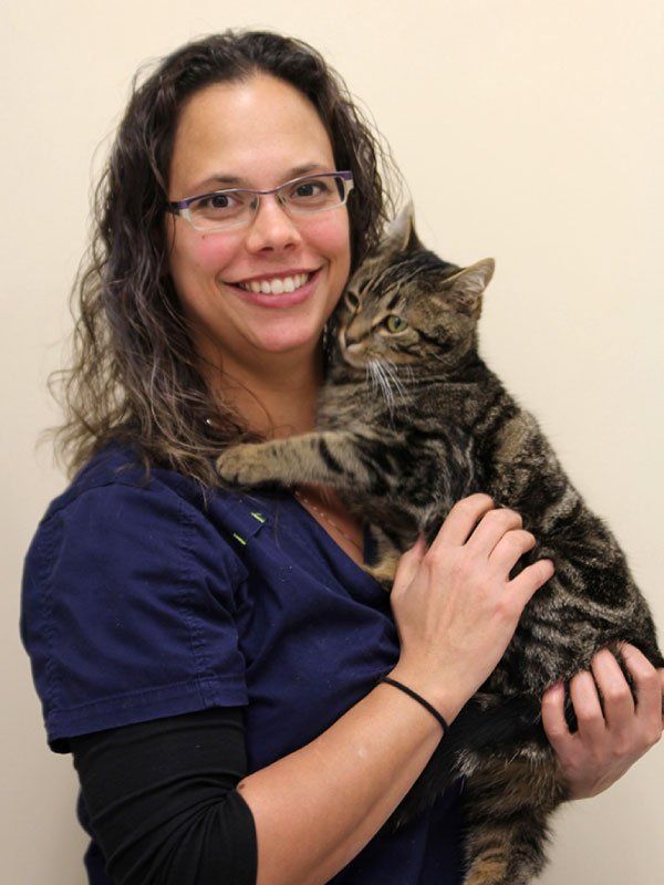 Woman in blue scrubs smiles while holding a tabby cat against a pale wall.