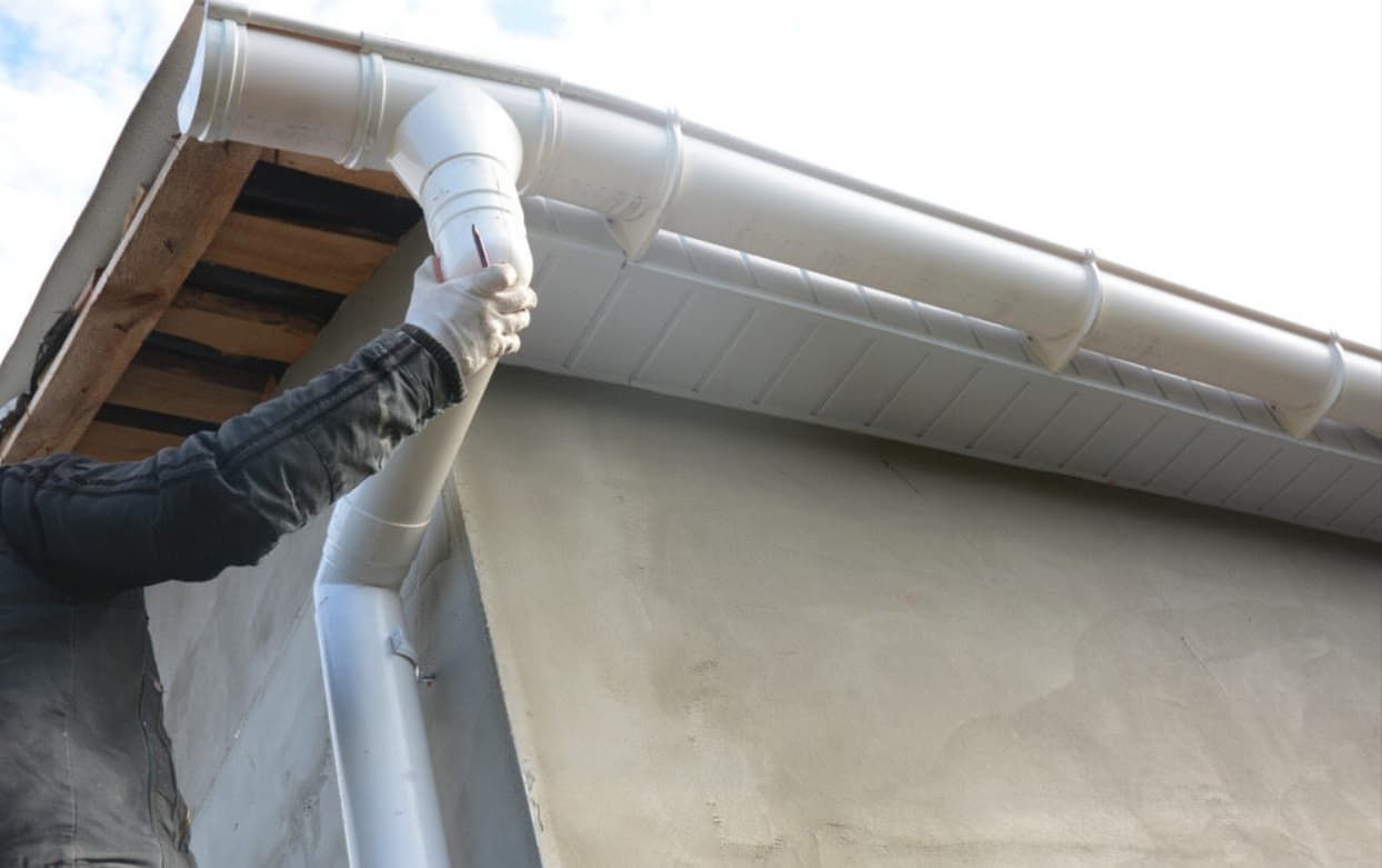 A Person is Installing a Gutter on the Side of a Building — GT Metal Roofing Solutions in Wollongong, NSW