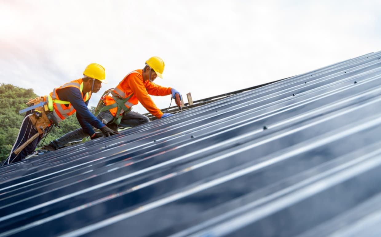 Two Construction Workers Are Working on a Metal Roof — GT Metal Roofing Solutions in Corrimal, NSW 
