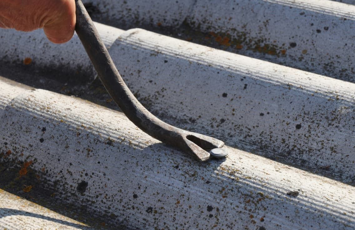 A Person is Using a Pry Bar to Remove a Nail From a Roof — GT Metal Roofing Solutions in Shoalhaven, NSW