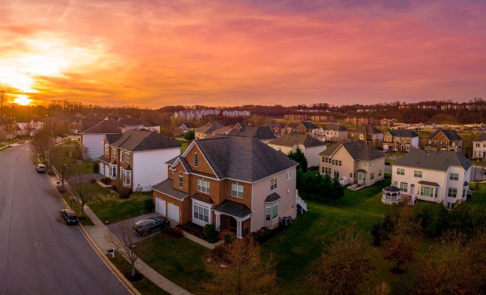 Sunset over suburban neighborhood with houses and green lawns.